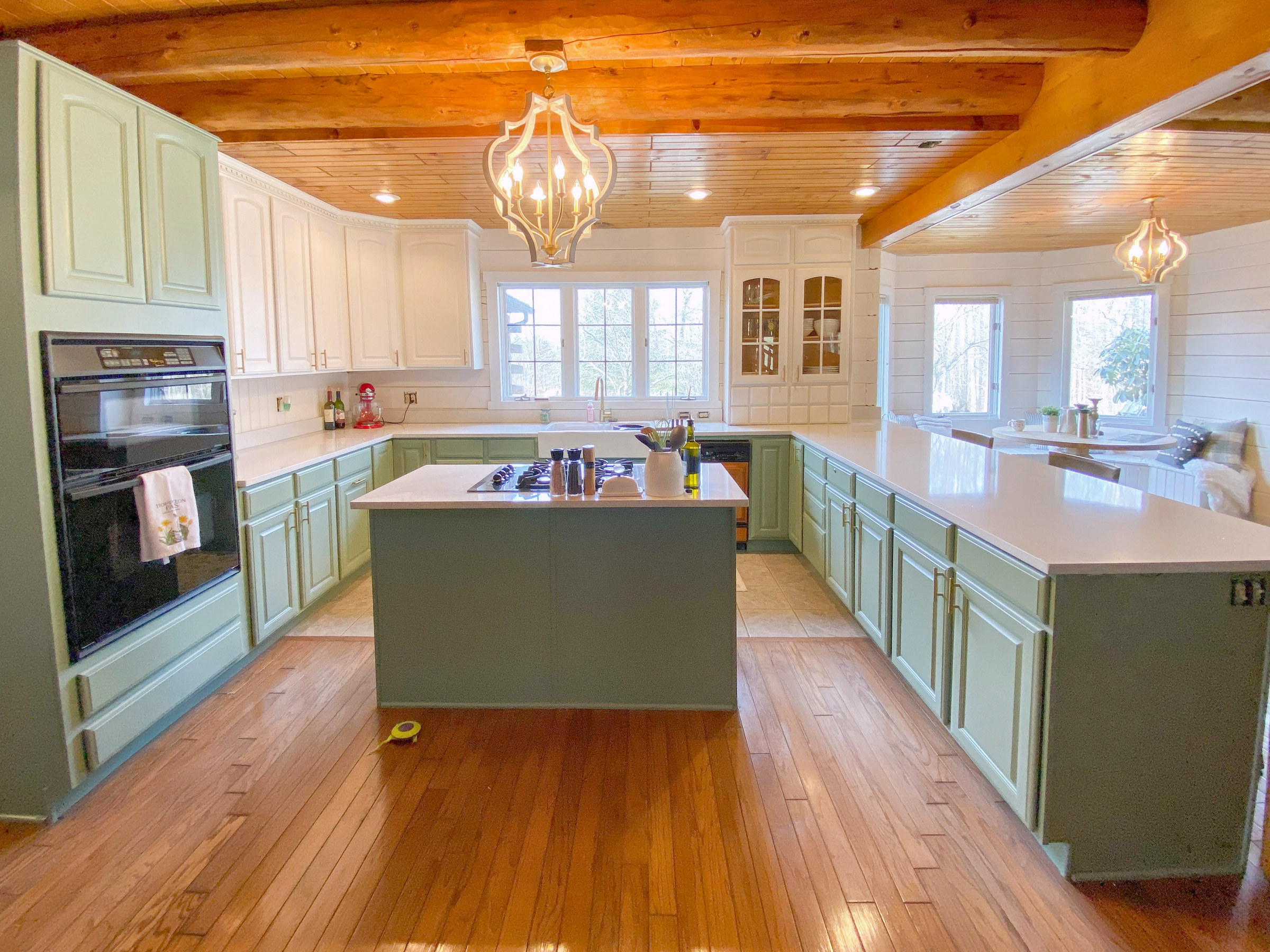 Sage green kitchen with a wood plank ceiling and a large island