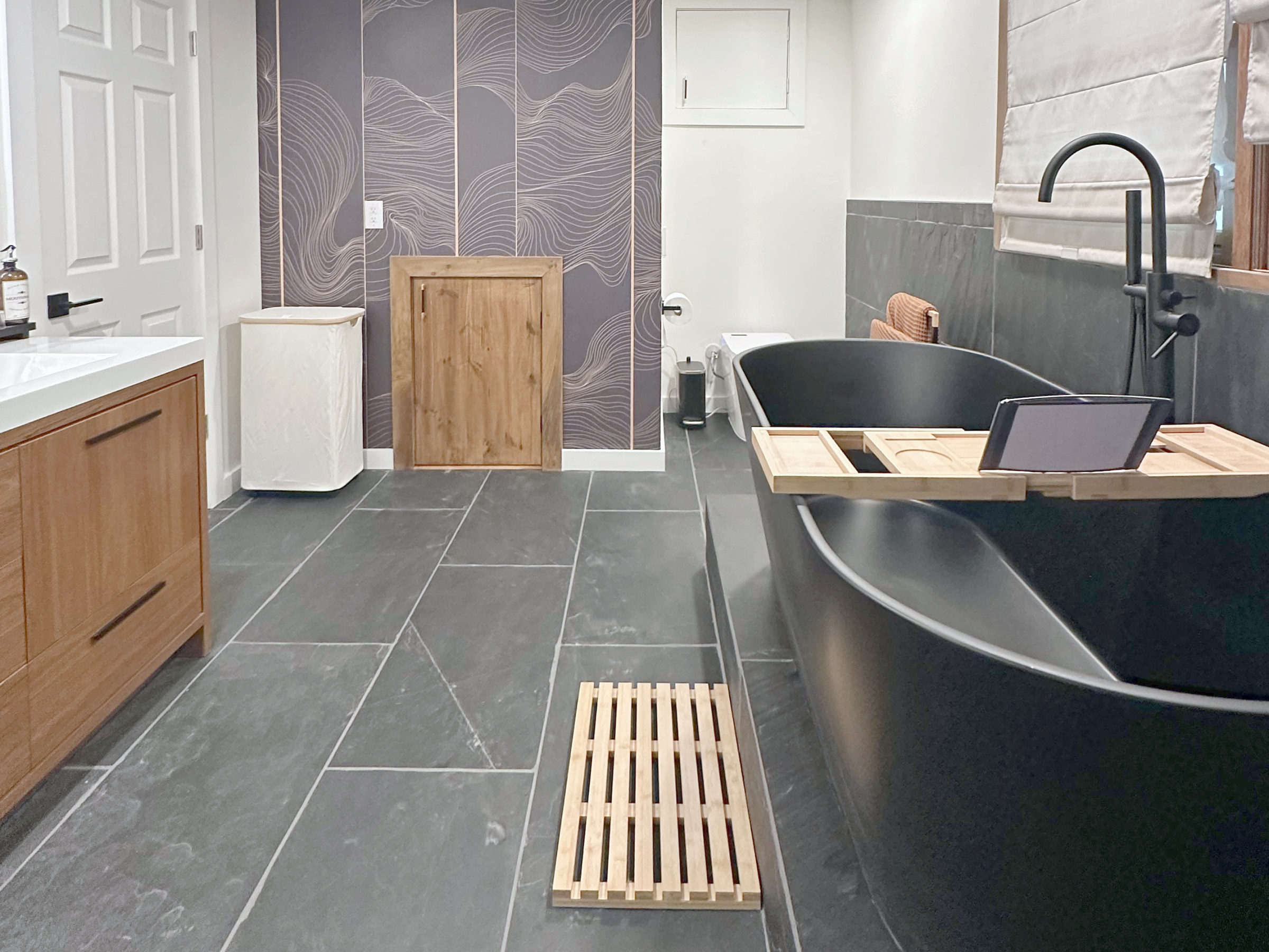 Bath with a black freestanding tub and dark tile floor